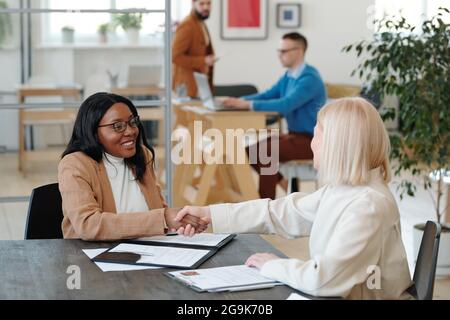 Cheerful female applicant and her new employer shaking hands over signed contract Stock Photo