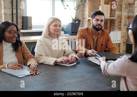 Young bearded businessman passing folder with contract to Asian female applicant Stock Photo