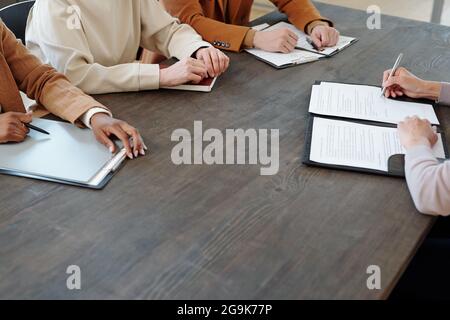 Young applicant signing document by table in front of three intercultural employers Stock Photo