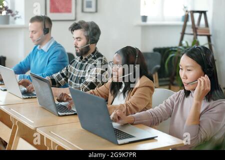 Multiracial operators sitting by desk in office during online consultation Stock Photo