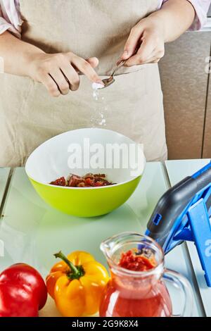 Teenager salt at salad using an online guide and views digital recipe on touch tablet while preparing healthy meal in the kitchen at home Stock Photo