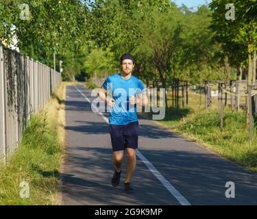 Athletic european man in sportswear jogging on road in green park on beautiful summer day Stock Photo