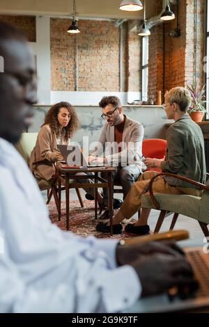 Young businessman computing by table among two female colleagues at meeting Stock Photo