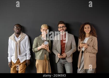 Young successful people with smartphones standing against grey wall Stock Photo