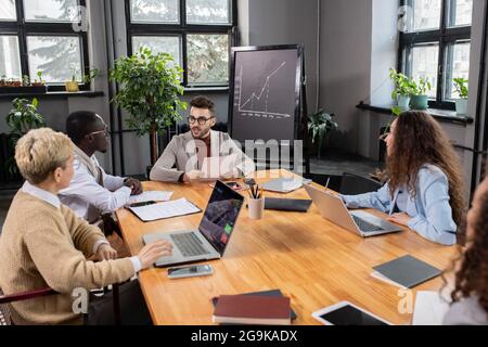 Coach with paper sitting by table in front of young intercultural managers Stock Photo