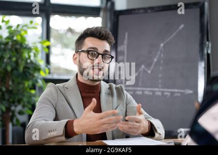 Confident teacher in eyeglasses and formalwear explaining his students important points of subject Stock Photo
