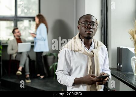 Young African businessman in eyeglasses and formalwear using smartphone Stock Photo