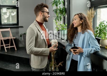 Two young smiling colleagues having discussion at break in office Stock Photo