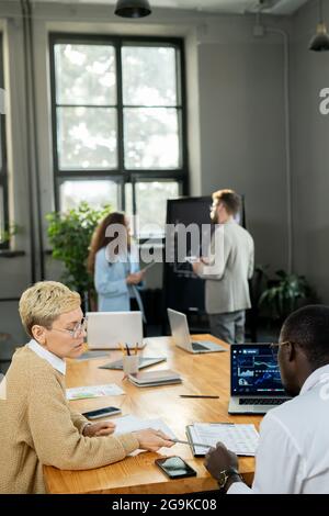 Young female economist presenting financial data to African male colleague Stock Photo