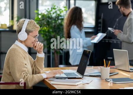 Young blond businesswoman in headphones looking at laptop display Stock Photo