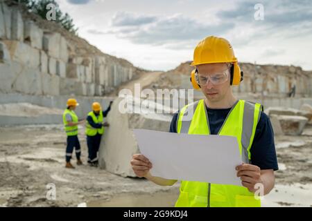 Young serious foreman in protective workwear looking at sketch on blueprint Stock Photo