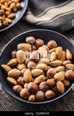 Unpeeled hazelnuts and almonds. Sweet nuts in bowl on black table. Stock Photo