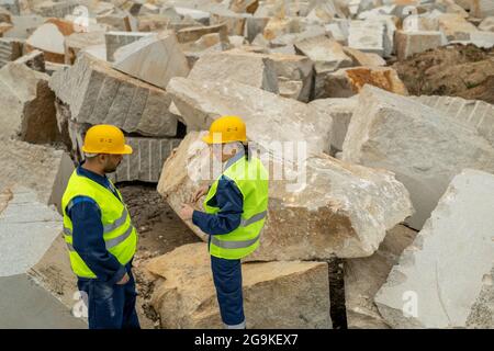 Two contemporary builders in workwear interacting between huge blocks at quarry Stock Photo