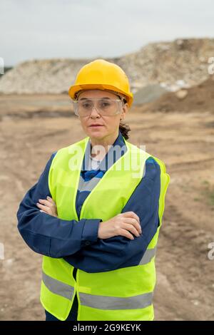 Female builder with crossed arms standing against quarry or construction site Stock Photo