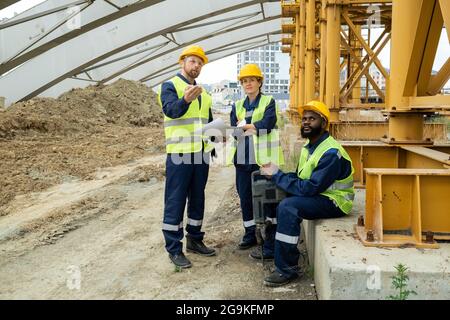 Group of construction workers looking at building and discussing project together on construction site Stock Photo