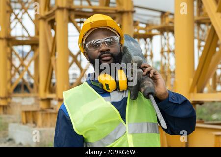 Portrait of African construction worker in work helmet looking at camera while working with drill on construction Stock Photo