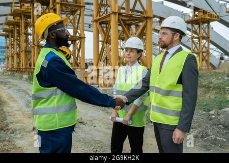 Construction workers shaking hands during meeting with colleague on construction site Stock Photo