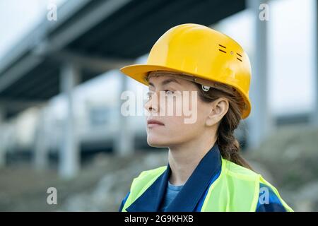 Close-up of young woman in work helmet looking away while standing on construction site outdoors Stock Photo