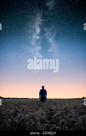 Man standing on wheat field under the stars of the milky way at night. Man looking at stars and dreaming. Stock Photo