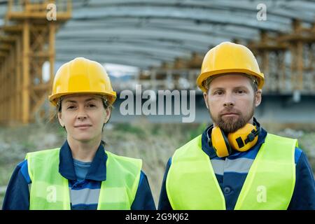 Portrait of two engineers in work helmets looking at camera while working together on construction site Stock Photo