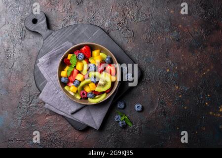 Natural organic food for healthy and dieting life. Top view of fresh fruit salad with kiwi, strawberry, blueberry, raspberry, peach and mint on dark c Stock Photo