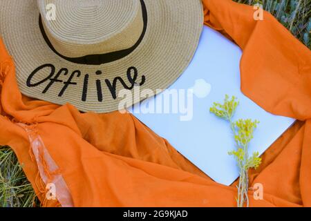 A straw hat with a written word Offline. An orange rag background, a gray laptop flatly. Lack of internet connection. Concept of break in work, busine Stock Photo