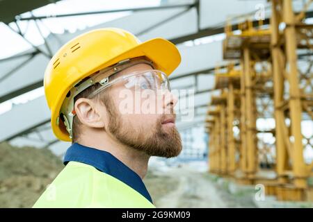 Close-up of engineer in work helmet and in protective glasses looking at construction of building outdoors Stock Photo