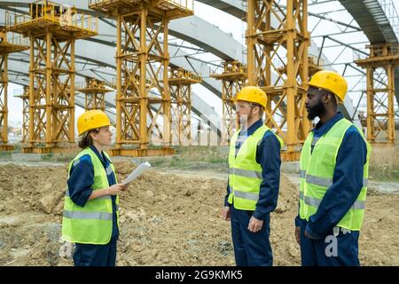 Foreman holding blueprint and giving the instruction to construction workers on the site Stock Photo