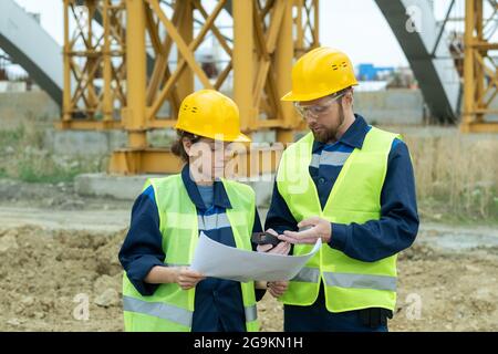 Two engineers working in team they standing on the site and discussing blueprint of future building Stock Photo