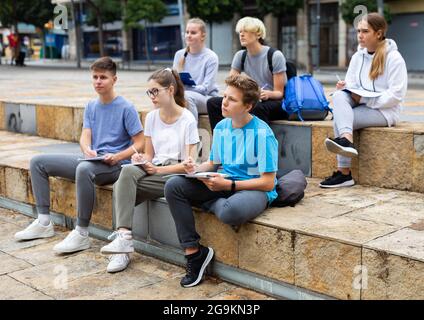 Teen students sitting with workbooks in schoolyard Stock Photo
