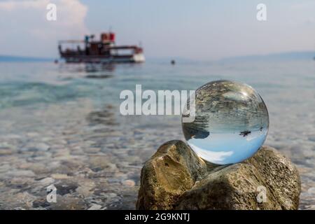 Crystal ball on stones near the sea. Original upside down view and rounded perspective of the sky, sea and boat. Original and engaging picture. Stock Photo