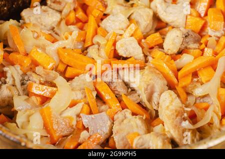 Meat with vegetables in the cauldron. Pork chunks mixed with onions and carrots. Cooking pilaf. Home cooking concept. Stock Photo