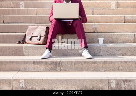 unrecognizable man working on his laptop computer sitting on a city staircase, technology and remote work concept Stock Photo