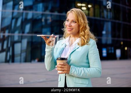 Secretary talks by phone outdoors near office center and holding cup of coffee. Stock Photo