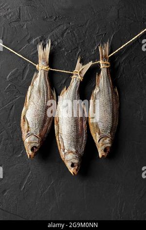 Dried salted roach fish hanging on rope on black wall Stock Photo