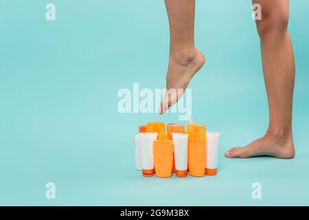 partial view of female legs near various containers with sunblock on blue Stock Photo