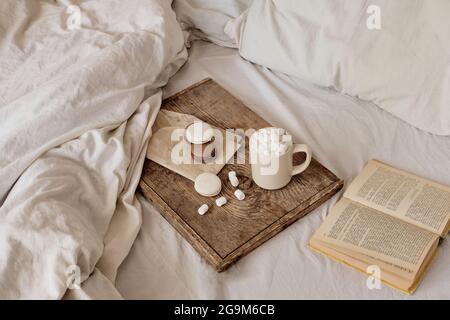 coffee with marshmallows and macaroons on a wooden tray, in bed. Aesthetically beautiful frame. Desserts in bed. hot chocolate with marshmallows Stock Photo