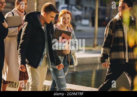 Cheerful students walking together outside in college. Boys and girls in university campus. Stock Photo