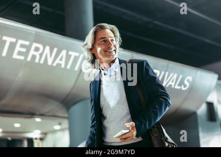 Happy business traveler walking at international airport. Businessman walking through airport terminal hallway. Stock Photo