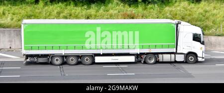 Side view of long green soft curtain easy access feature on articulated trailer with white hgv lorry truck cab & driver travelling along UK motorway Stock Photo