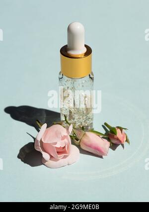 bottle of 24k gold serum on a blue background with rose flowers. The concept of skin care at home Stock Photo