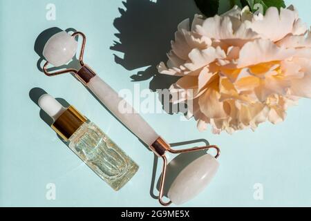 Massage roller for the face made of rose quartz with bottle of 24k gold serum on a blue background. The concept of skin care at home Stock Photo