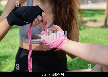 Unrecognizable person helping other to put on muay thai hand wraps sitting on grass in a park. Sport outdoors. Stock Photo