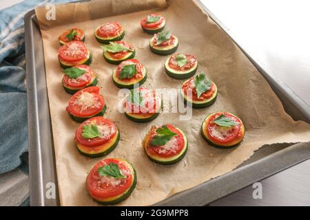 Mini pizza snack from the oven, homemade from slices of zucchini, tomato and parmesan with parsley garnish on a baking tray, selected focus, narrow de Stock Photo
