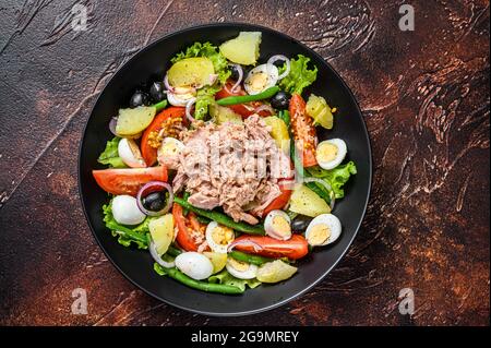 Healthy hearty salad with tuna, green beans, tomatoes, eggs, potatoes and black olives in a plate. Dark background. top view Stock Photo