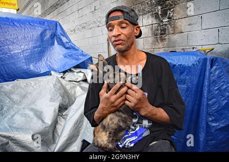 Skid Row, Downtown Central Los Angeles, California, USA, June 2021. Anthony, a homeless veteran, who actually holds a job, feeds his cats.Los Angeles is facing a humanitarian crisis it has never seen before as homelessness and drug abuse grow in the area named 'Skid Row.' The Covid-19 pandemic added to the problem as property prices went through the roof, unemployment claims increased and illegal immigration caused explosion in homelessness. An estimated 70,000 people roam the streets and camp out in the city near the exits and entrances to the freeways, under bridges and overpasses, in parks Stock Photo