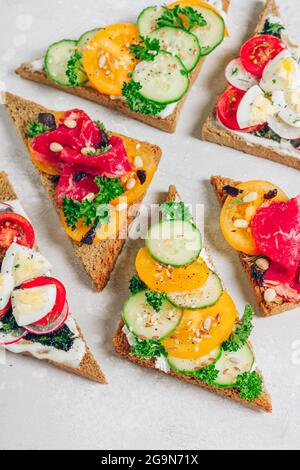 Fresh wholegrain toasts with healthy ingredients - prosciutto, tomatoes, eggs, and veggies. Italian bruschetta sandwich, greens and seeds on top Stock Photo