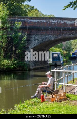 man sitting in a chair fishing on a summers day on the towpath of the bridgewater canal in manchester. angler or fisherman on the bridgewater canal. Stock Photo