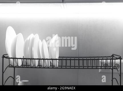 Clean white dishes drying on metal dish rack on bright light kitchen background photo Stock Photo
