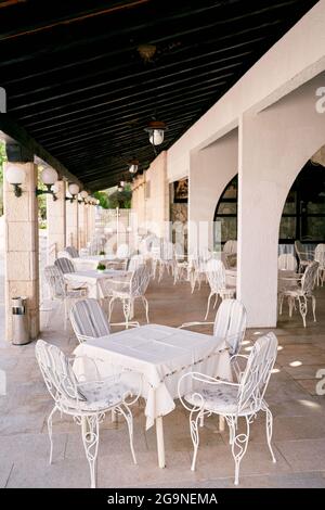 White tables with tablecloths and chairs stand on the covered veranda of the restaurant with columns Stock Photo